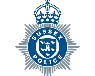 The Sussex Police logo, featuring a blue and silver eight-pointed star with a crown on top, and a circular emblem in the center displaying "Sussex Police" around a shield with six birds and a cross.