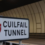 A sign reading "Cuilfail Tunnel" with a red shield emblem, positioned in front of the entrance to a modern, curved tunnel.