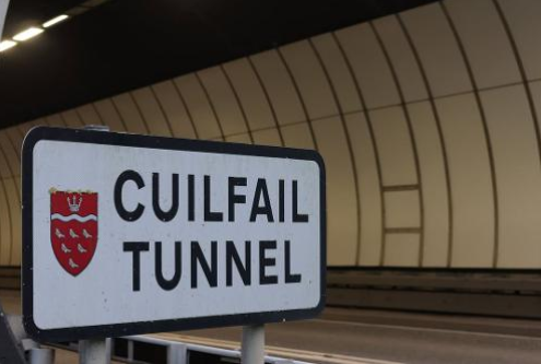 A sign reading "Cuilfail Tunnel" with a red shield emblem, positioned in front of the entrance to a modern, curved tunnel.