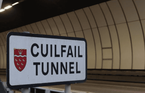 A sign reading "Cuilfail Tunnel" with a red shield emblem, positioned in front of the entrance to a modern, curved tunnel.